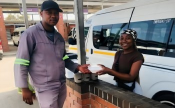 A young woman poses outside a taxi stand handing goods from her coffee business to a male customer.