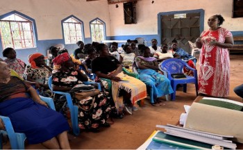 A group of people sit listening to a female trainer during a training session in Kenya.