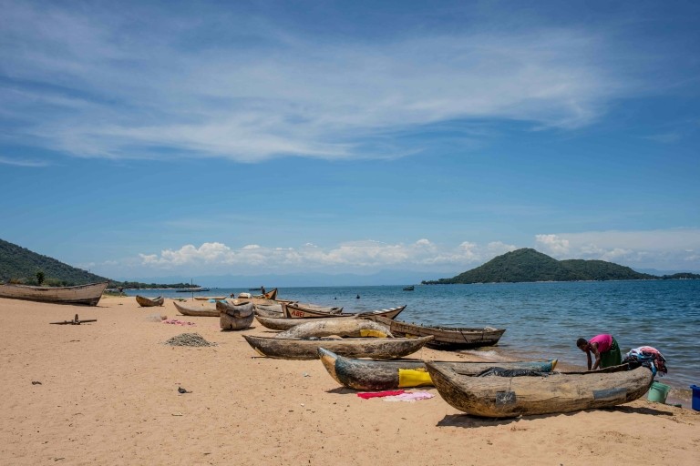 Women reach into boats on a beach in Malawi. 