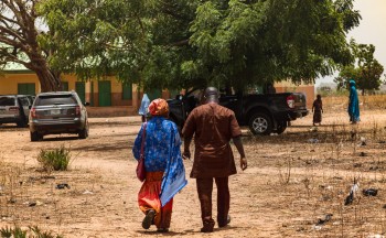 A man and woman walk together holding hands outside on a dirt path in Nigeria.