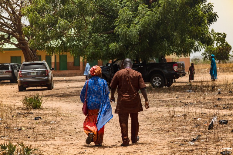 A man and woman walk together holding hands outside on a dirt path in Nigeria.