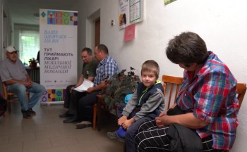 A young boy waits to see a doctor from the mobile health team, which brings essential health care services directly to remote communities. Photo credit: Pact.