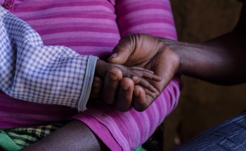 A child in Tanzania holds the hand of a case worker. Credit: Michael Goima/Pact