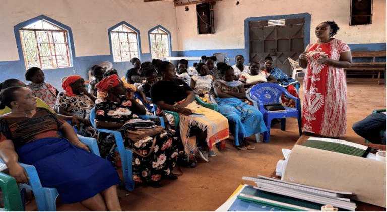 A group of people sit listening to a female trainer during a training session in Kenya.